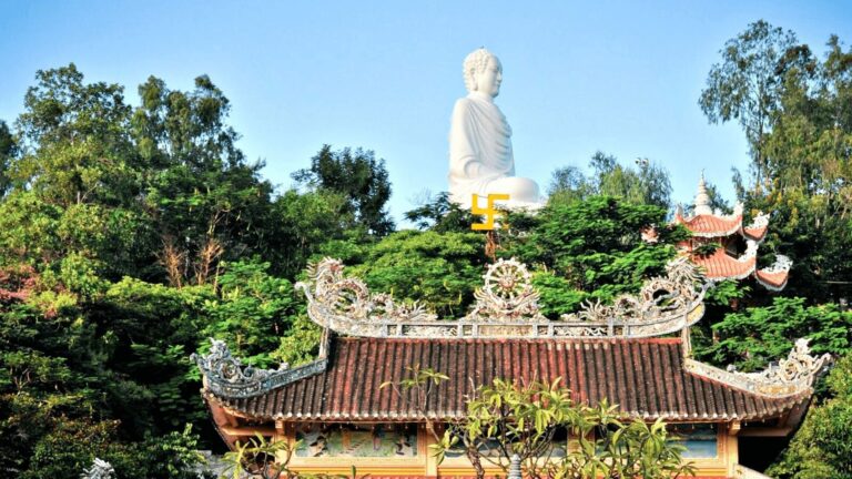 The White Buddha statue at Long Son Pagoda surrounded by lush green trees in Nha Trang.